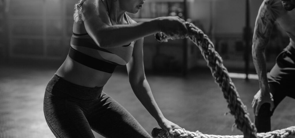 Woman training with fit man in gym using battling ropes